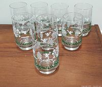 Set of 8 clear drinking glasses with white and green farmhouse-themed designs arranged on wood surface.