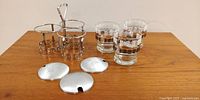Full view of the set showing the four Libby glasses, metal carrying caddy with handle, and four detachable metal lids placed on the table