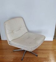 Front and side angles of an off-white leather low-back swivel chair on chrome base on wooden floor against a white wall.