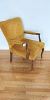 Full view of vintage mustard-yellow armchair showing entire chair with wooden legs and arms, mustard upholstery, and fabric buttons on backrest.