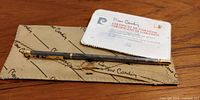 Vintage Pierre Cardin pen laid across sheath and certificate on wooden surface. Shows pen, sheath, and certificate in single frame to confirm inclusion.