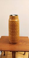 Full view of tall mustard yellow textured ceramic floor vase on wooden table