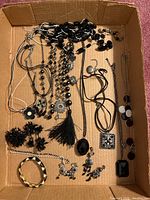 Overhead image showing multiple pieces of costume jewelry in a cardboard box including necklaces, earrings, brooch, and bracelet.