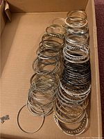 Overview photo of multiple metal bangle bracelets arranged in a box, showcasing various sizes and finishes.
