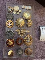 Overview of all 16 brooches with various designs including emblems, crosses, and eagles on gray surface.