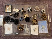 Tray displaying 20 assorted brooches and packaged earrings, including black rhinestone pieces, floral designs, and heart-shaped items.