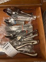 Photo of assorted stainless steel flatware pieces grouped and bundled in plastic wrap in a wooden drawer.