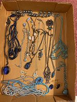 Box containing multiple costume jewelry pieces including necklaces, bracelets, and earrings displayed inside a cardboard box.