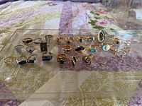 Full view of 28 costume rings arranged in rows showing various colors and designs including blue stones and silver and gold tones.