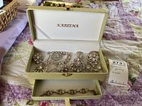 Jewelry box open showing nine brooches inside and one bracelet in drawer below