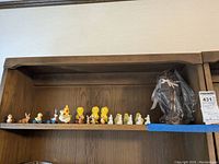 Shelf with multiple small plastic and ceramic Easter figurines including ducks and bunnies, and a wrapped ceramic chocolate bunny figurine.