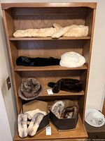 Wooden shelf with seven fur collars arranged on shelves and in boxes, two faux fur hats included, showing colors from beige to dark brown and white.