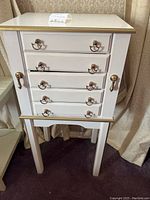 Front view of white and gold jewelry cabinet with four drawers and side cabinets