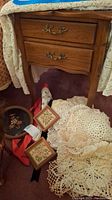 Photo of crocheted doilies, two small framed needlepoint floral artworks, and some fabric items like apron and tablecloth visible partly.