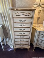 Front view of the tall lingerie chest showing the nine drawers with decorative handles and gold trim.