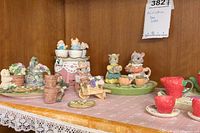 Photo of multiple miniature tea sets including bunnies sitting in teacups, garden pots, and strawberry-themed cups on a lace-covered table