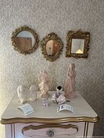 Three ornate mirrors with gold-tone frames, one round, one oval, one rectangular, hanging on decorative wallpaper.