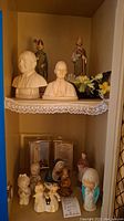 Two shelves with various religious figurines including busts of Popes, angel figures, and saints.