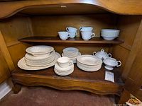Display of teacups, saucers, various plates, cream and sugar pots inside wooden cabinet.