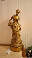 Full view of the gold-colored statue of a woman holding cherries on a decorative base