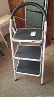 Front view of the metal step stool ladder showing 3 black steps and white frame with padded handle.