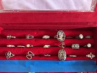 Full view of 20 rings displayed on red ring tray, showing a variety of designs including large stones, filigree details, ornate and plain silver bands, some marked 925 sterling silver.