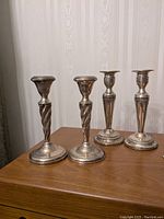 Front view of two pairs of sterling silver candlesticks, one pair twisted spiral design, the other pair baluster shape