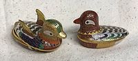Side view of two bird-shaped cloisonné boxes showing detailed enamel colors and patterns on each bird.