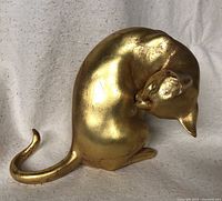 Front and side view of gold gilded cat sculpture showing the curling tail and grooming pose.