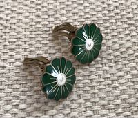 Pair of green guilloche enamel floral clip-on earrings on fabric background showing front sides.