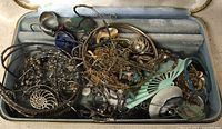 Overhead photo of the open jewelry box showing various jewelry items inside including bracelets, earrings, chains, and a fan-shaped accessory.