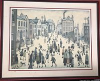 Framed print of "A Village Square" showing village street scene with numerous figures and buildings, signed by L.S. Lowry in lower right corner.