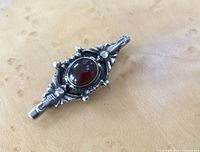 Close-up of the front of the brooch, showing detailed silver floral design and oval garnet cabochon.