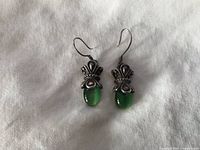 Pair of sterling silver earrings with green oval Limori stones displayed flat on a white fabric background, showing front and back views.