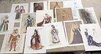 Photo showing many of the 26 vintage lithographs with costume designs laid out on a table, featuring diverse character depictions in period attire.