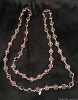 Full view of purple faceted crystal necklace laid on black background showing multiple linked stones and length.