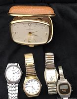 Full display of all five timepieces: four wristwatches and one travel clock in beige case