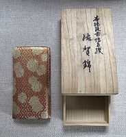 Front and top view of the Saga Nishiki purse with original wooden box next to it. The box is open and empty.