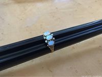 Close-up side angle of the vintage ring highlighting the three opalescent glass stones surrounded by small faux pearls and the detailed gold-tone band.