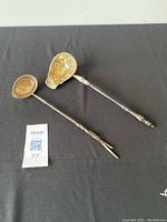 Two Georgian silver hot toddy ladles displayed on black fabric, showing differences in handle designs and basin shape.