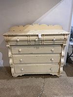 Front view of the antique Canadian pine chest of drawers showing the cream-colored paint, porcelain knobs, and decorative backboard.