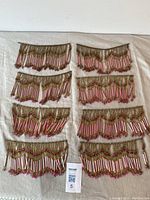 Eight pieces of antique glass beaded fringe trim laid out on a beige fabric surface, showing overall design and size.