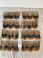 Full view of all eight black glass beaded fringe pieces arranged on beige fabric, showing the set and condition.