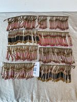 Photo showing eight strands of vintage glass bead fringes laid out on a cloth surface with pink and black beads accented by gold and green small beads
