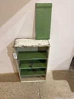 Front view of painted antique wooden shelf with green removable panel leaning on wall.