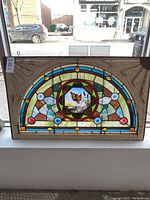 Full front view of the arched stained glass window in its original painted wooden frame.