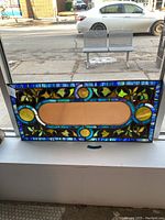 Full view of the stained glass window panel placed on a window ledge, showing colorful border and central plain area.