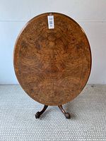 Front view of the oval tilt top table showing inlaid matchbook veneer detail on walnut surface.
