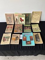 Front view of 13 Arts & Crafts furniture reference books arranged in three rows on a black cloth against a white wall.