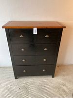 Front view of the chest of drawers showing natural wood top and black painted drawers with metal shell handles.